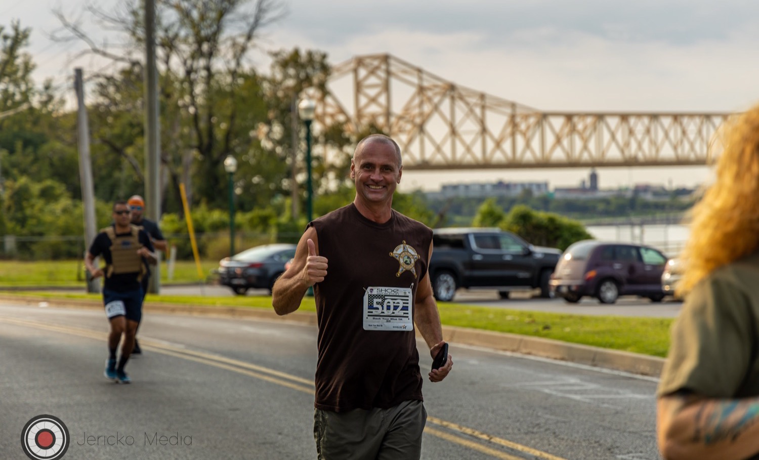 A runner mid-race at the Back Your Blue 5K with the river bridge behind