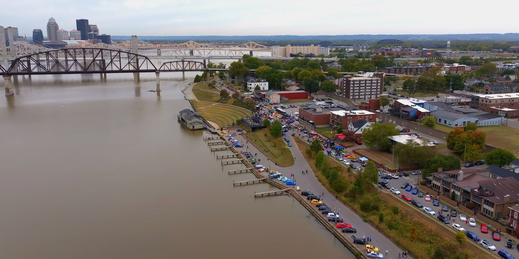 Aerial view of downtown Jeffersonville's riverfront on the Ohio River, with a crowd along Riverside Drive and the bridges behind